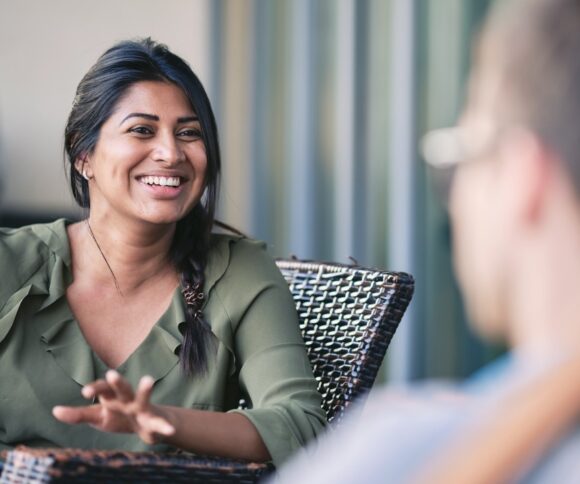 The picture shows a dialog situation with the focus on a smiling women sitting in a chair.