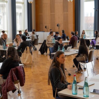 The picrure shows a room with many tables at each of which are two people talking.