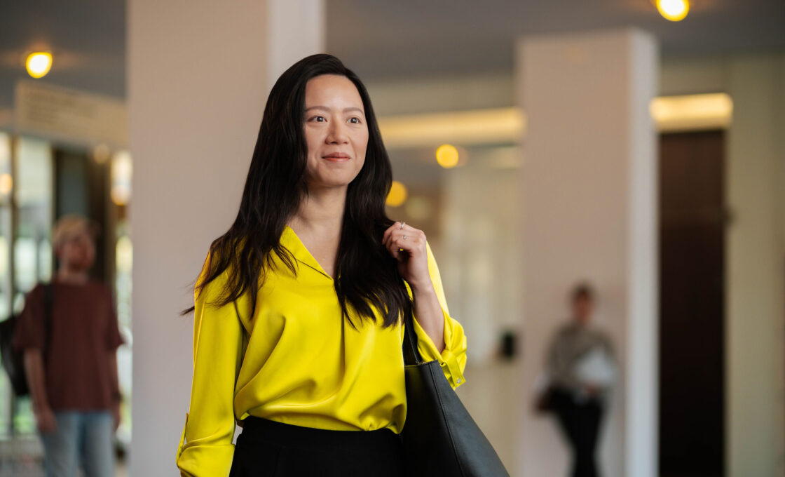 Female student in bright yellow attire standing attentively in a modern foyer at HHL.