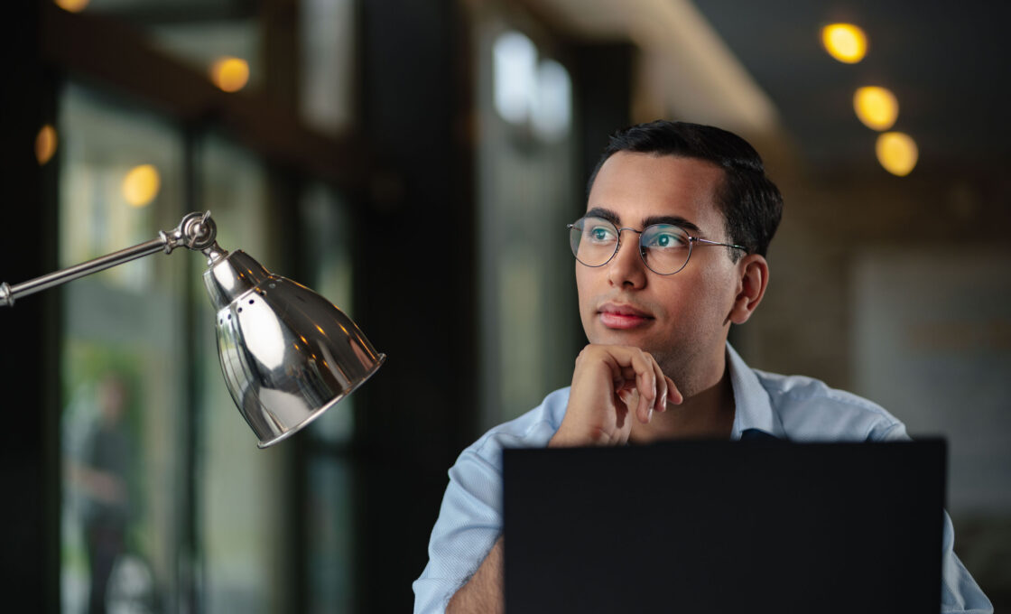 Male student with glasses looking attentively past a laptop screen.