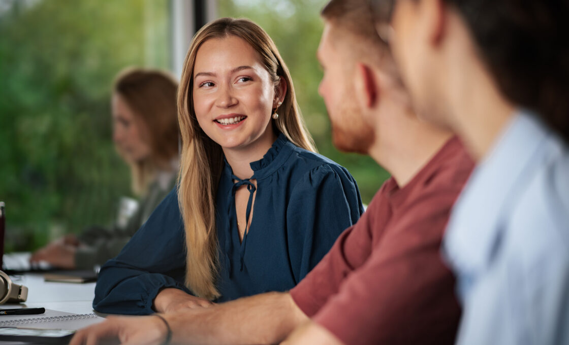 Female student in a dark blouse sitting in a discussion group with fellow students.
