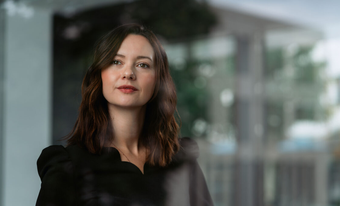 Female student with brown hair looking outside through a reflective glass window.